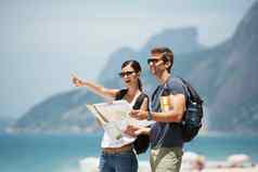 特殊的年轻的夫妇持有地图指出海滩