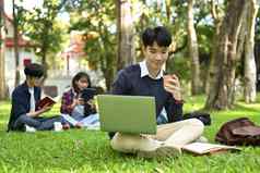 微笑亚洲男人。大学学生坐着校园草坪上工作移动PC电脑教育生活方式概念