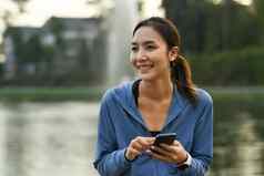 迷人的亚洲女跑步者体育运动衣服聪明的电话早....锻炼公园
