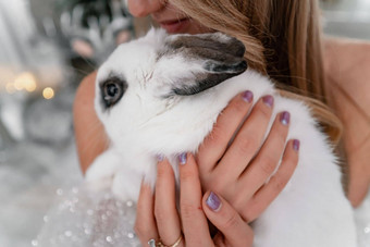 女人持有白色兔子象征一年特写镜头美丽的年轻的金发女郎女人持有兔子闪亮的衣服坐在圣诞节装饰房间