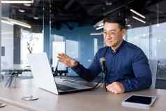 年轻的亚洲男人。办公室说话麦克风视频调用移动PC