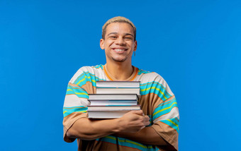 年轻的男人。学生持有堆栈大学书大学图书馆蓝色的背景快乐的家伙微笑快乐研究生教育在国外概念
