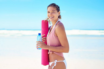 加入海滩瑜伽年轻的女人持有瑜伽席站海滩