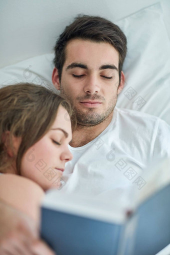 享受幸福朴素年轻<strong>的</strong>夫妇阅读书床上妻子睡觉胸<strong>部首</strong>页