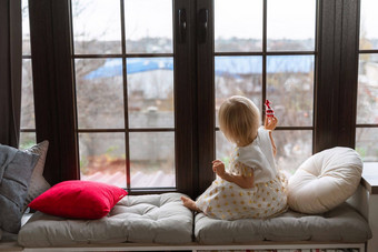 女孩年坐在窗台上金发女郎女孩白色衣服窗台上窗口持有糖果手