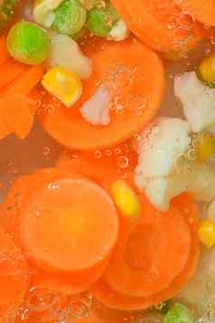 特写镜头新鲜的汤蔬菜胡萝卜豌豆菜花玉米白色背景汤蔬菜胡萝卜豌豆菜花玉米沸腾水白色背景特写镜头垂直图像前视图平设计
