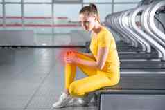 年轻的女人运动服装疼痛膝盖培训健身房女孩坐着地板上触碰膝盖疼痛
