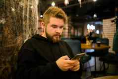 英俊的集中的家伙使钱事务应用程序移动电话互联网坐着咖啡馆街晚上千禧男人。阅读文本消息智能手机