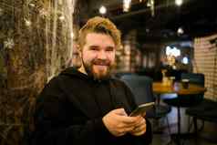 肖像快乐的家伙使钱事务应用程序移动电话互联网坐着咖啡馆街晚上千禧男人。阅读文本消息智能手机