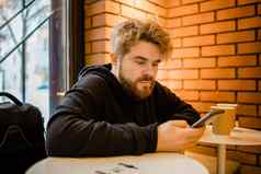 肖像快乐的家伙使钱事务应用程序移动电话互联网坐着咖啡馆街晚上千禧男人。阅读文本消息智能手机
