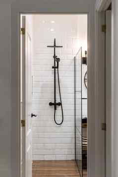 淋浴区域浴室门口走廊白色砖墙油漆反映明亮的光灯天花板墙黑色的金属水龙头玻璃栏杆一边