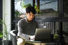 英俊的亚洲男人。自由职业者移动PC工作在线项目远程户外咖啡馆