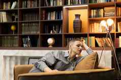 成熟的女人灰色的衬衫坐在舒适的舒适的椅子背景首页图书馆