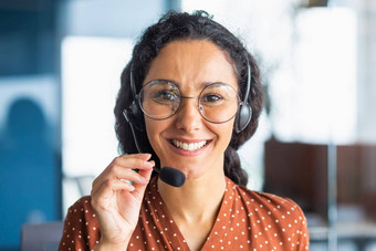 关闭肖像拉丁美国女人内部现代办公室耳机视频调用女人微笑相机办公室工人客户支持科技热线服务电话