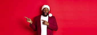 圣诞节聚会，派对假期概念兴奋黑色的男人。显示广告指出手指促销提供站圣诞老人他红色的背景