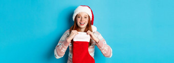 美丽的红色头发的人女孩圣诞老人他开放圣诞节长袜惊讶接收圣诞节礼物站蓝色的背景