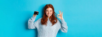 快乐红色头发的人女孩毛衣显示信贷卡标志推荐银行提供站蓝色的背景