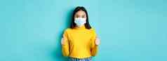 科维德社会距离流感大流行概念支持亚洲女人推荐促销活动穿医疗面具显示拇指站蓝色的背景