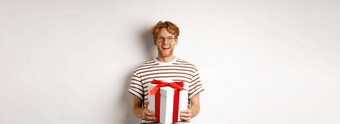 情人节一天假期概念快乐的年轻的男人。持有礼物盒子微笑感激的接收礼物站白色背景
