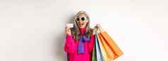 时尚的亚洲祖母太阳镜购物假期出售持有纸袋塑料信贷卡站白色背景