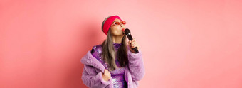 时尚的亚洲高级女人唱歌首歌执行卡拉ok麦克风站聚会，派对装人造皮毛外套粉红色的背景