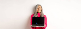 电子商务概念美丽的亚洲高级女商人显示空白移动PC屏幕微笑站粉红色的毛衣白色背景