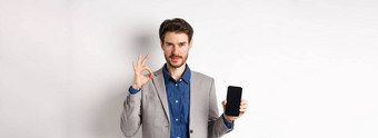 电子商务在线购物概念自信英俊的业务男人。西装显示标志空智能手机屏幕推荐应用程序白色背景