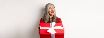 快乐假期概念快乐的亚洲高级女人给红色的礼物盒子微笑祝贺情人节一天站白色背景
