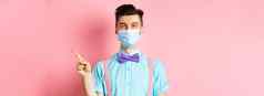 科维德流感大流行健康概念微笑高加索人男人。医疗面具指出手指显示广告站粉红色的背景