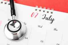 听诊器医疗7月桌子上日历红色的背景时间表检查健康的概念
