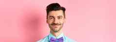 特写镜头微笑帅的男人。胡子穿蝴蝶结衬衫站快乐的粉红色的背景