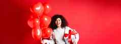 兴奋美丽的女人庆祝情人节一天假期持有礼物盒子浪漫的心气球惊讶相机站红色的背景