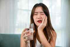 亚洲年轻的女人敏感的牙齿持有玻璃冷水