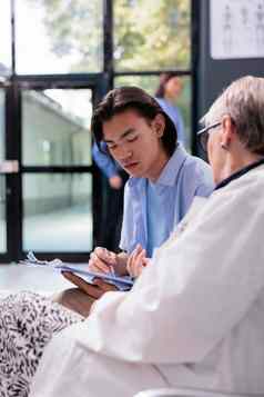 年轻的亚洲病人签署医疗文档上了年纪的医生解释健康护理治疗