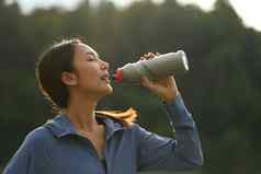 女人喝水瓶休息慢跑公园晚上健康的生活方式健身概念