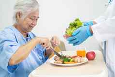 亚洲高级上了年纪的夫人女人病人吃早餐蔬菜健康的食物希望快乐坐着饿了床上医院