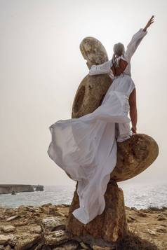 女人站石头雕塑使大石头穿着白色长衣服背景海天空衣服发展风