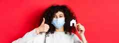 真正的房地产流感大流行概念特写镜头女人推荐机构穿医疗面具显示拇指纸房子断路红色的背景