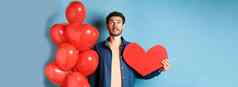 情人节一天爱概念男人。梦幻脸持有浪漫的礼物气球红色的心断路站蓝色的背景