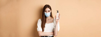 流感大流行医疗保健概念女人有关科维德穿医疗面具显示瓶手洗手液站米色背景