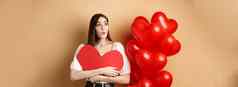 情人节一天爱概念感兴趣温柔的女孩拥抱大红色的心断路站气球标志哇米色背景