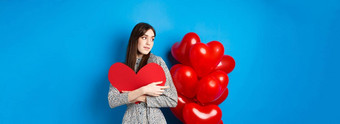 情人节一天美丽的浪漫的女人沉思的气球拥抱大红色的心微笑等待爱蓝色的背景