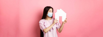 真正的房地产流感大流行概念兴奋亚洲女孩医疗面具很高兴纸房子断路购买财产站粉红色的背景