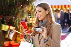 圣诞节女人携带购物袋户外美丽的微笑女孩支付礼物在线移动电话信贷卡模糊人圣诞节市场背景