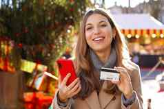 圣诞节女人微笑相机持有智能手机信贷卡手圣诞节树市场背景