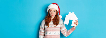假期广告片真正的<strong>房地产</strong>概念可爱的红色头发的人女人<strong>圣诞</strong>老人他毛衣显示纸房子模型公寓提供站蓝色的背景