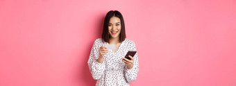 美丽的亚洲女人输入信贷卡信息移动电话应用程序购物在线<strong>支付订单</strong>智能手机站粉红色的背景