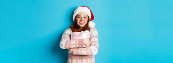 冬天庆祝活动概念梦幻红色头发的人女孩圣诞老人他拥抱圣诞节礼物微笑快乐站蓝色的背景