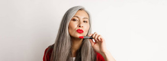 美化妆概念美丽的亚洲上了年纪的女人皱<strong>纹嘴唇</strong>显示红色的口红时髦的相机白色背景
