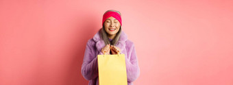 购物时尚概念快乐亚洲高级女人时尚的衣服快乐很高兴站黄色的纸袋微笑粉红色的背景